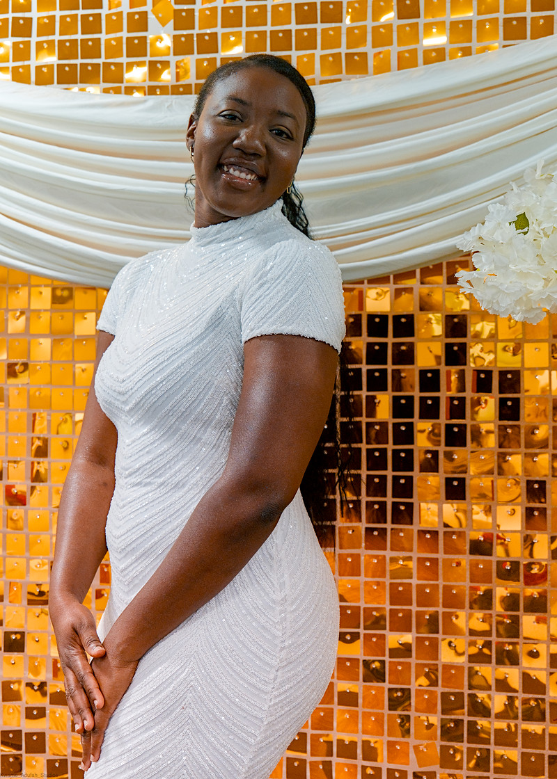 A guest in a white dress smiles over her shoulder in front of a gold sequin wall