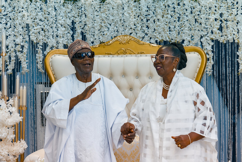 The celebrant and his wife dance in front of the floral wall and gold throne